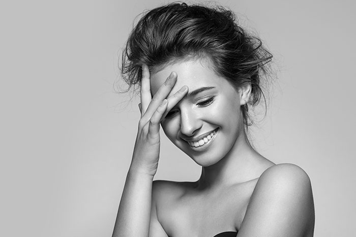 Black and white, girl smiling and looking down with hand on her forehead