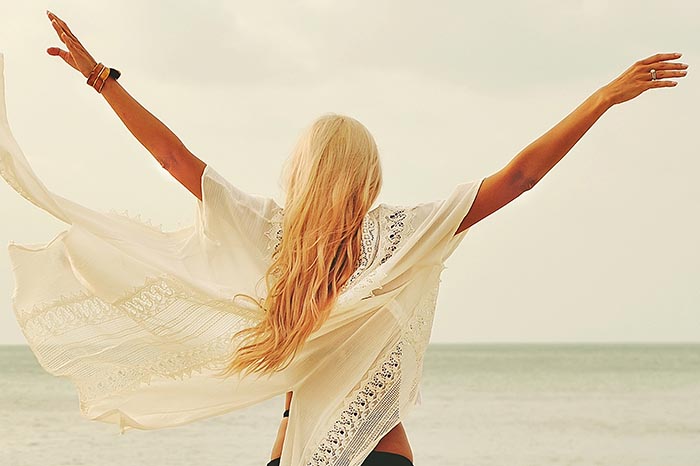 Woman at the beach, hands in the air, back facing the camera